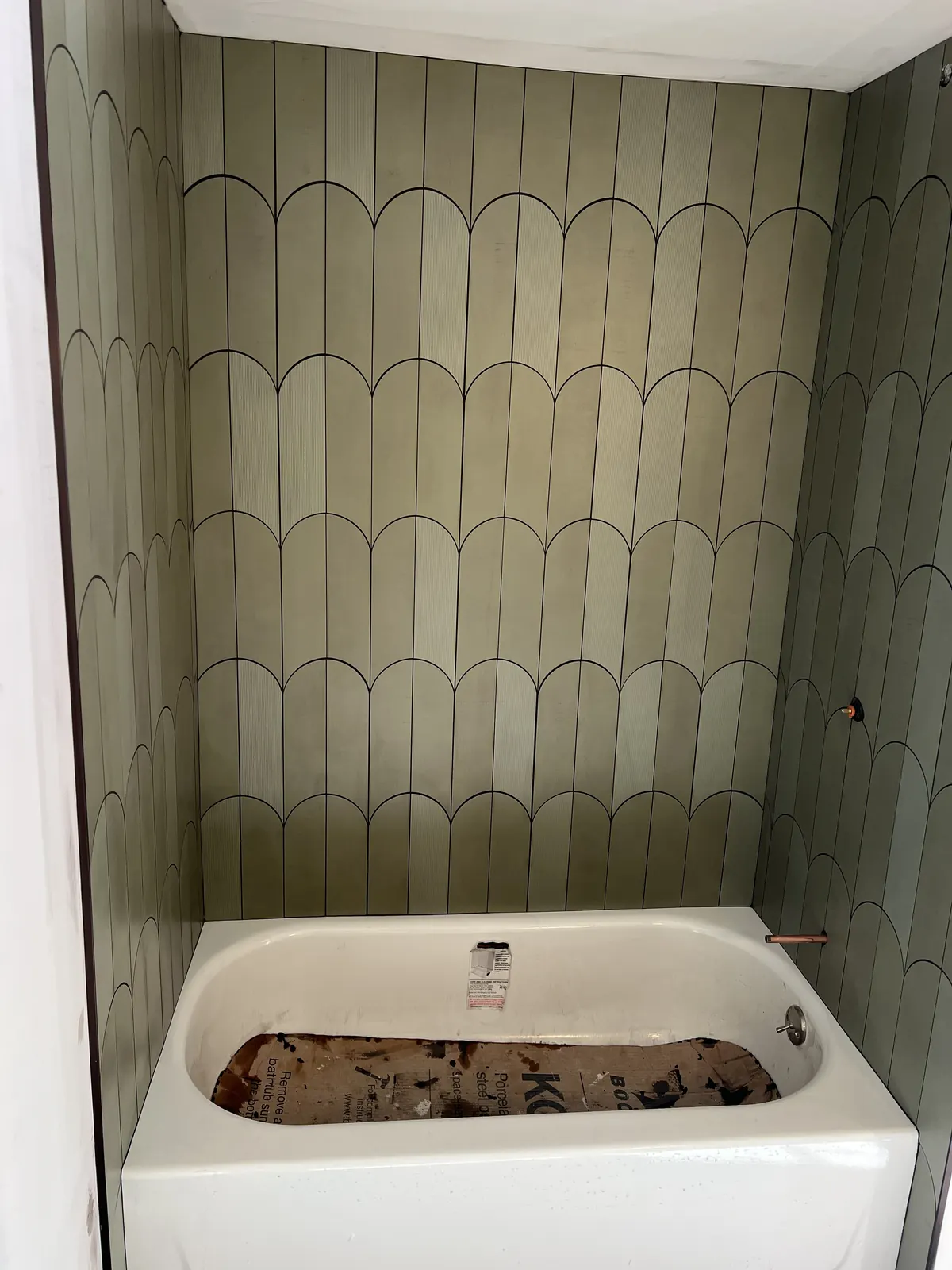 Bathtub surround with sage green arched ceramic wall tile pattern