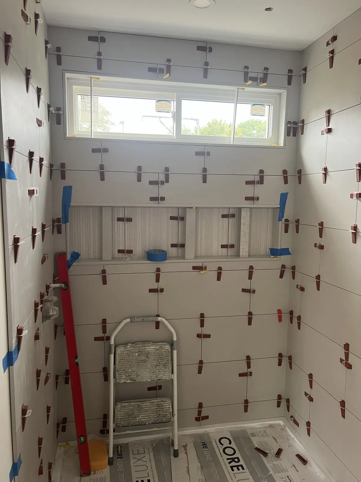 Large-format bathroom wall tile installation in progress with leveling clips and a recessed shelf