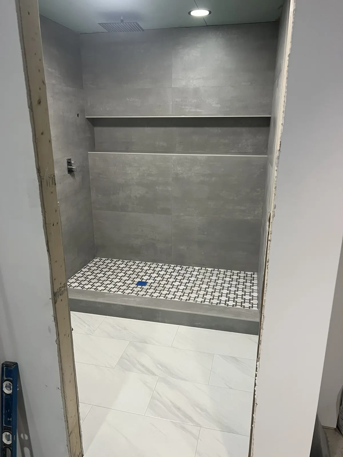 Walk-in shower with gray large-format wall tile, patterned mosaic shower floor, and marble-look bathroom floor