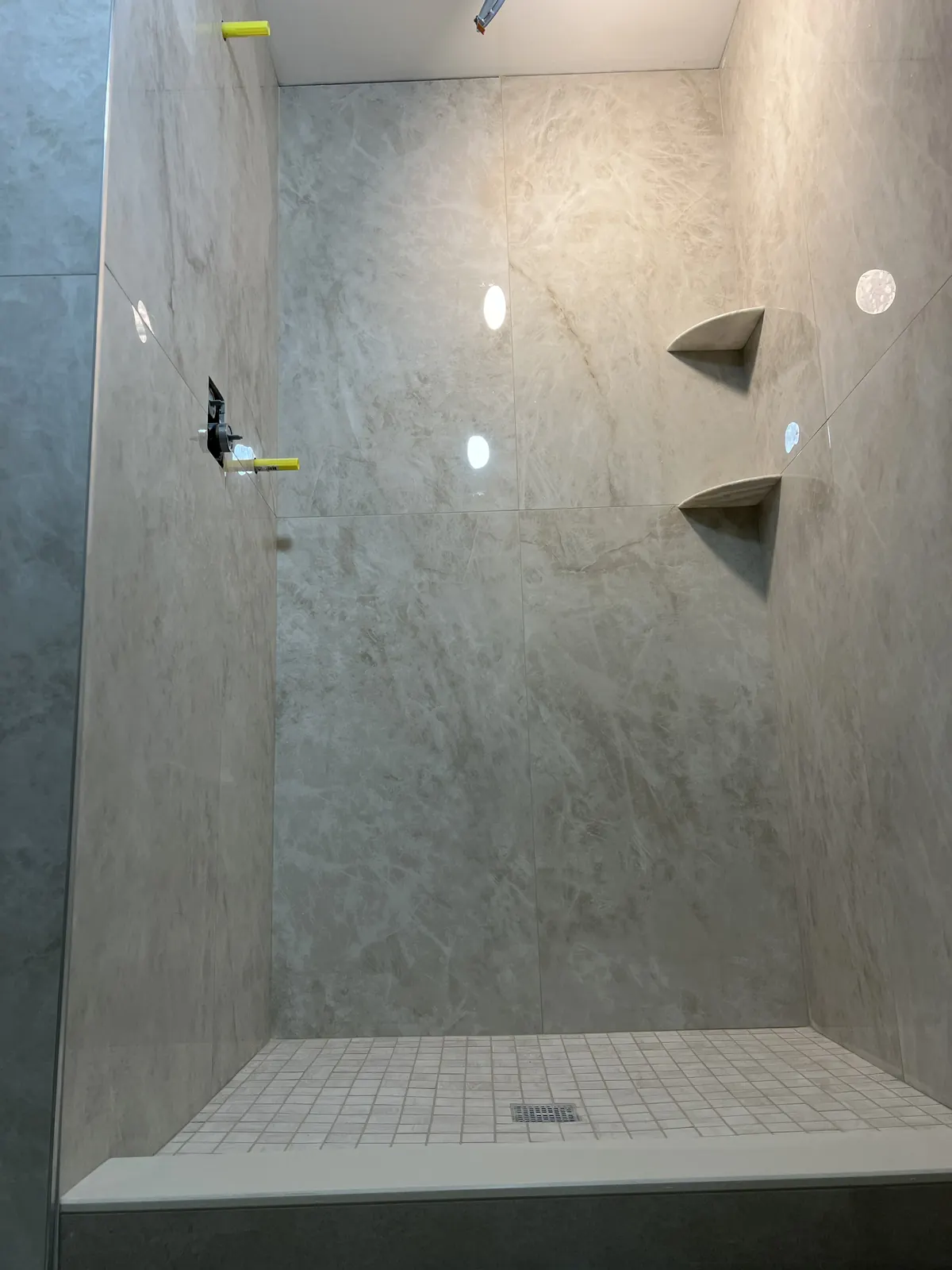 Stone-look porcelain walk-in shower with mosaic floor and corner shelves