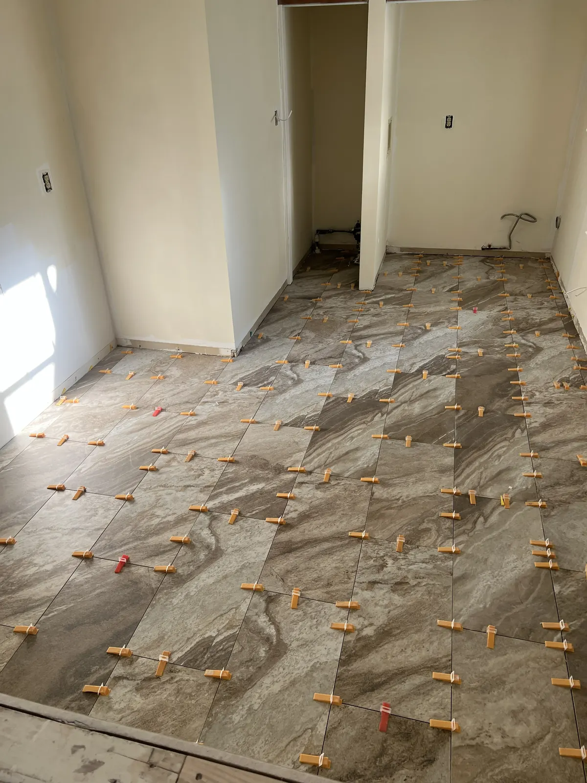 Large-format marble-look porcelain floor tile installation with leveling spacers